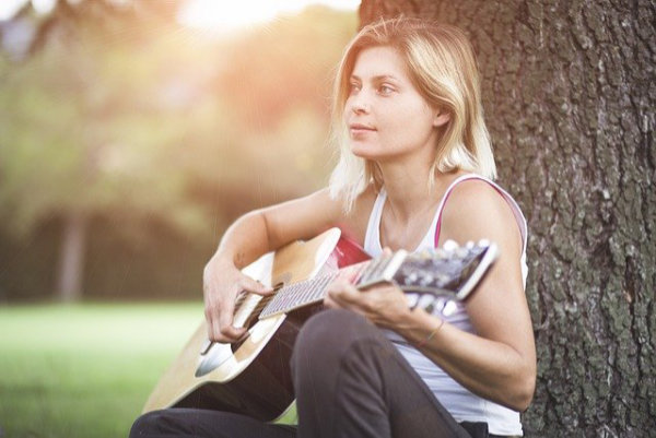 Singen lernen an deinem Lieblingsort Frau beim Gesangstraining online mit Gitarre in einem Park